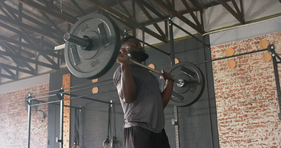 After gripping rack barbell African American man pressing overhead, dropping into back squat at gym. Strength, fitness, workout, training, athletic, motivation, exercise