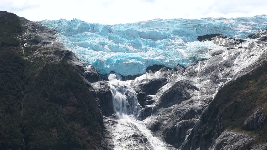 Majestic glacier with waterfall cascading down rocky cliffs in remote wilderness area