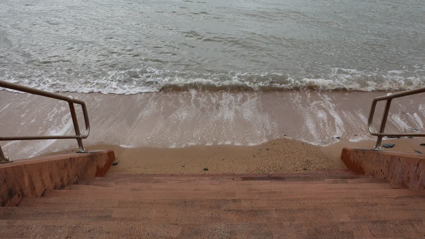 Gentle ocean waves lapping at a sandy beach at the base of concrete steps