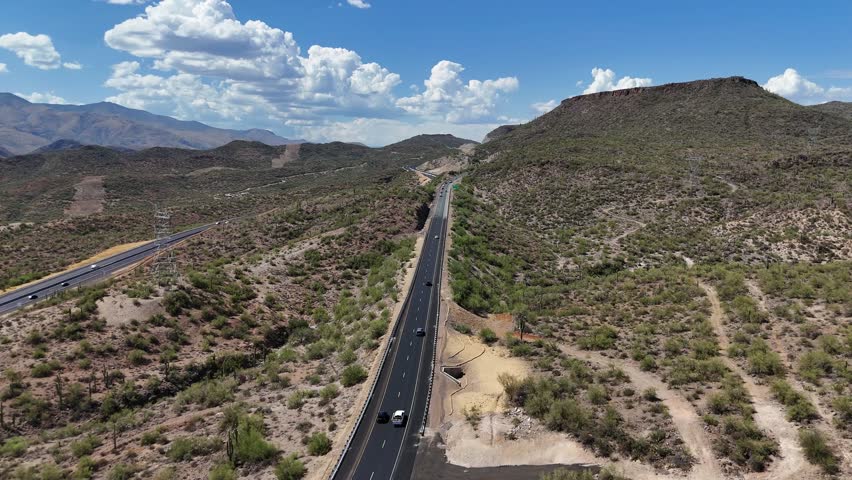 Drone Flying over Interstate 17 North of Black Canyon City in Arizona. Few cars driving on highway. Buttes, hills, mountains and blue sky with large clouds in background