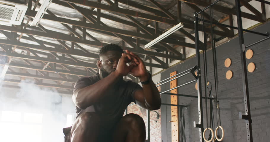 Squatting low, African American man jumping onto plyometric box in gym boosting power. Fitness, training, athletic, explosive, strength, dynamic, gym