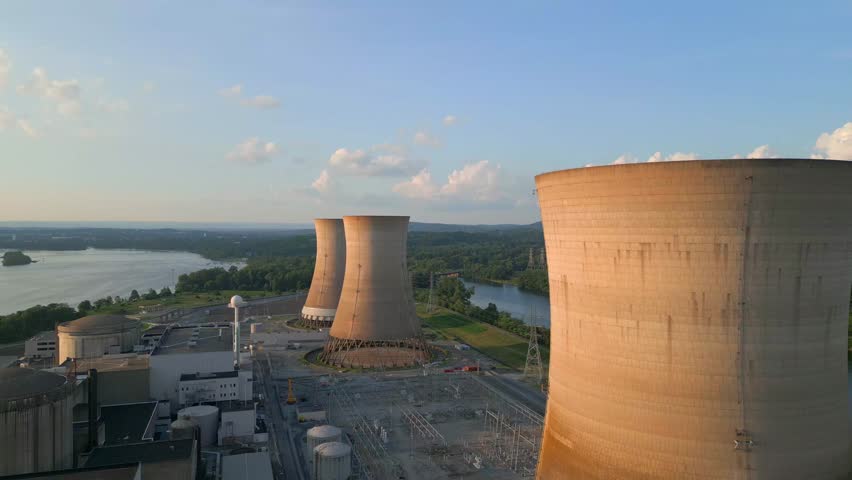 Aerial drone video of a nuclear power plant and its cooling towers during sunset.