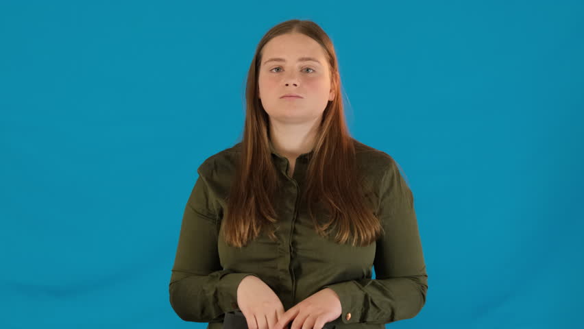 Young woman shows paper bag with red bow on blue background. Confident female proposes festive gift package for special occasions
