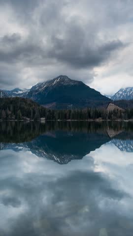 4K portrait shot of snowy Tatra Mountains, calm Štrbské Pleso lake, pine forest, moody sky, and sunlit trees—perfect for travel, nature, resort, meditation, and landscape footage.