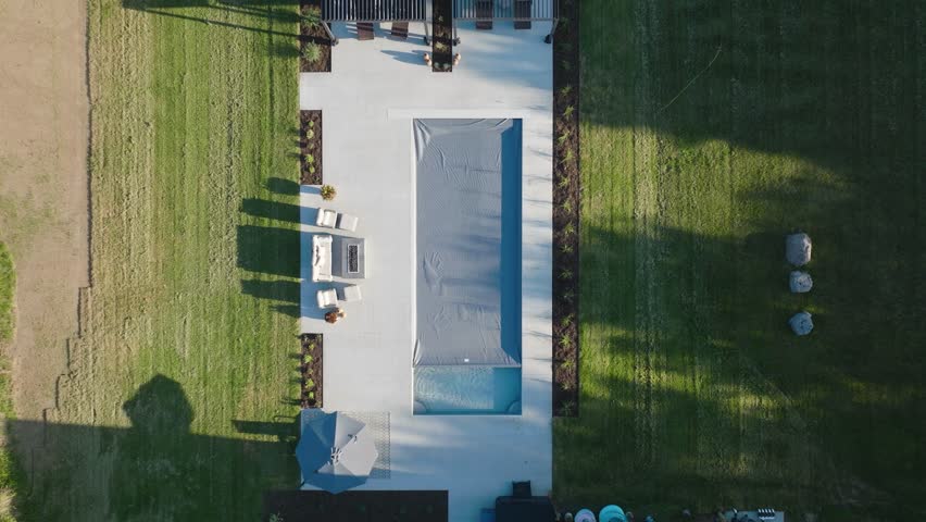 Overhead views of a modern backyard pool with cover mid-retraction and neat landscaping.