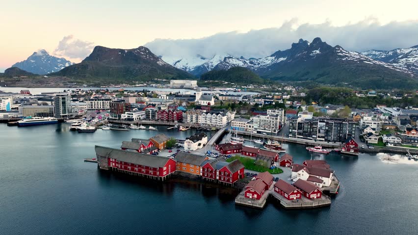 Drone flies toward Lamholmen in Svolvaer showing city, harbor and mountains under midnight sun