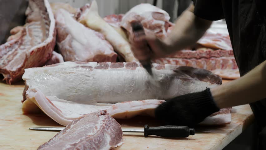 A butcher cuts a pig carcass with a knife at a sausage factory. Sausage production.