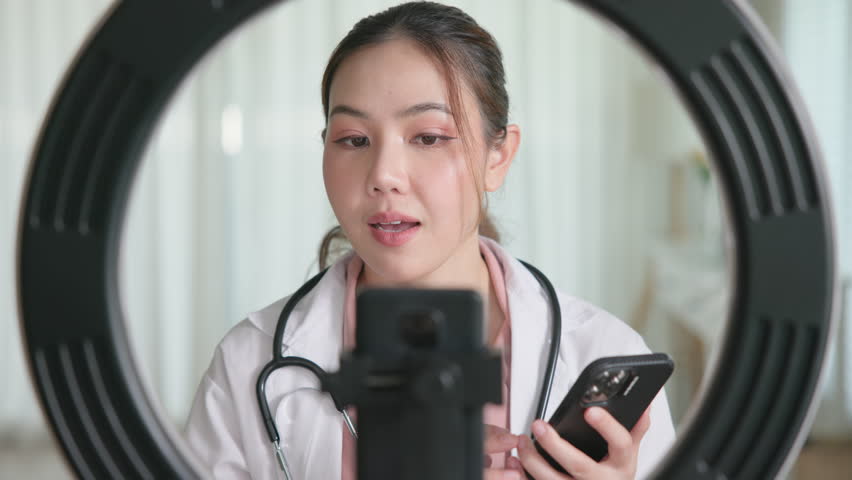 Young adult woman Gen Z asia people anti aging expert modern nurse live talk viral video selfie camera on mobile phone app mental health care. Online sharing digital virtual asian vlogger filming.