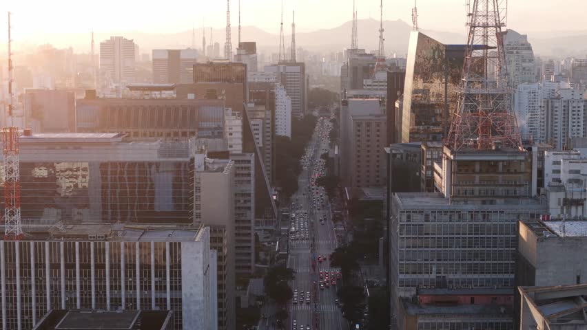 View of Paulista Avenue at dusk with heavy traffic and long buildings, captured with a telephoto lens to emphasize depth and city scale.