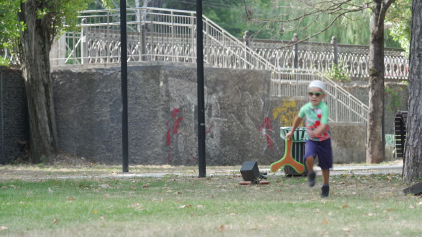 A child is focused on handling a boomerang, preparing to throw it in a green park. The natural outdoor setting highlights a moment of playful learning and enjoyment in Simferopol, Crimea.