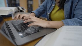 A focused young Asian female student with glasses uses a laptop and books to do research in a library, representing digital learning, hybrid education, and student lifestyle concepts. - Powered by Shutterstock - Get 15% off with code: PIKWIZARD15
