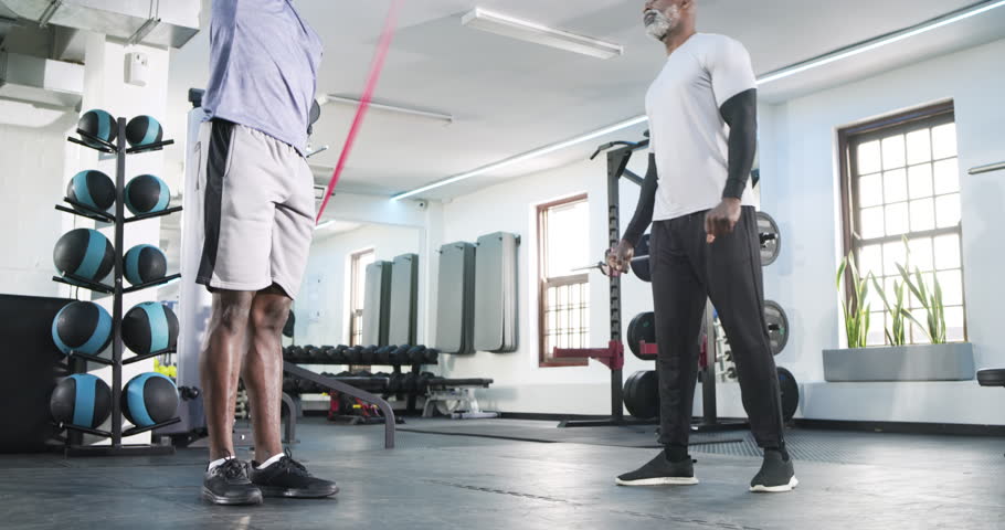 Grabbing pink band, African American men doing rotations, assisted tricep stretch for warmup at gym. Training, fitness, strength, flexibility, rehabilitation, exercise, health