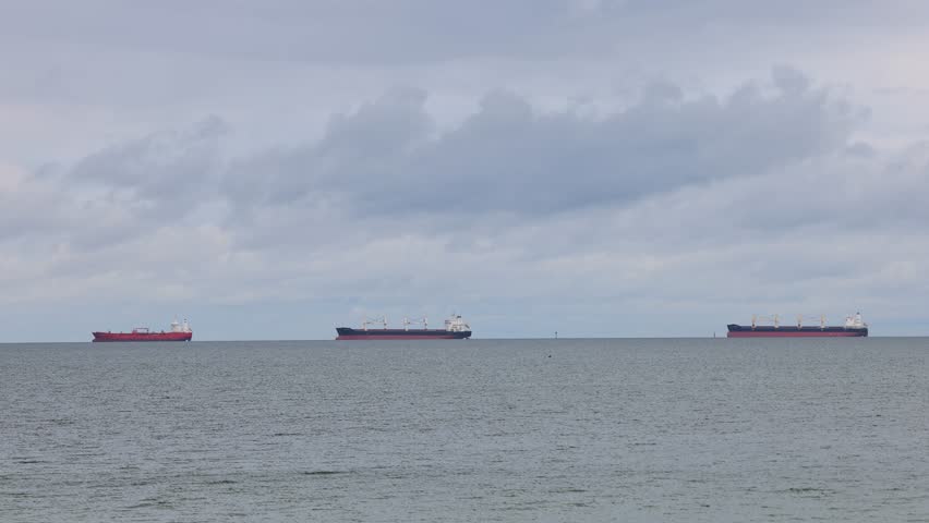 The coast of the Baltic Sea in northern Poland. Three ships dot the horizon under a cloudy sky, sailing serenely on the water. Minimalist seascape conveys tranquility.