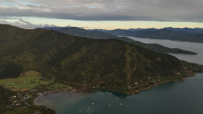 Marlborough Sounds and Cook Strait at sunrise, lush green hills, and sailboats on calm water, Picton, New Zealand. Aerial drone panoramic view