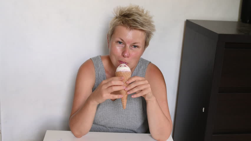 Short cut blonde woman eating ice cream cone at home in living room	