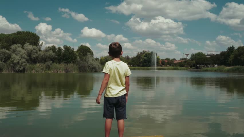 Young Boy Watching Lake Fountain on Sunny Dock
