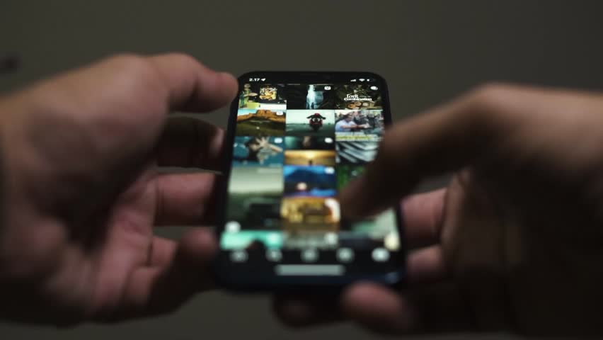 Close-up shot of hands using smartphone surfing in internet. Scrolling news feed with pictures or photo gallery choosing content for social media or instagram. Mobile gadget and technology concept