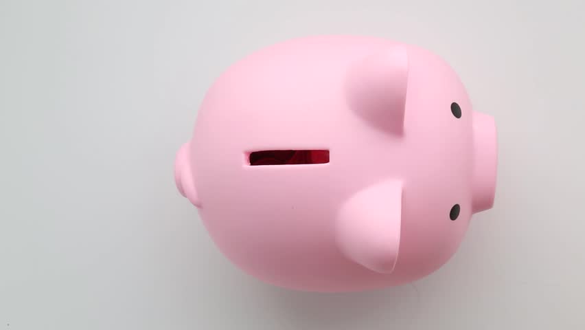 Human hand carefully placing multiple coins into pink ceramic piggy bank slot with audible metallic sounds on neutral background surface