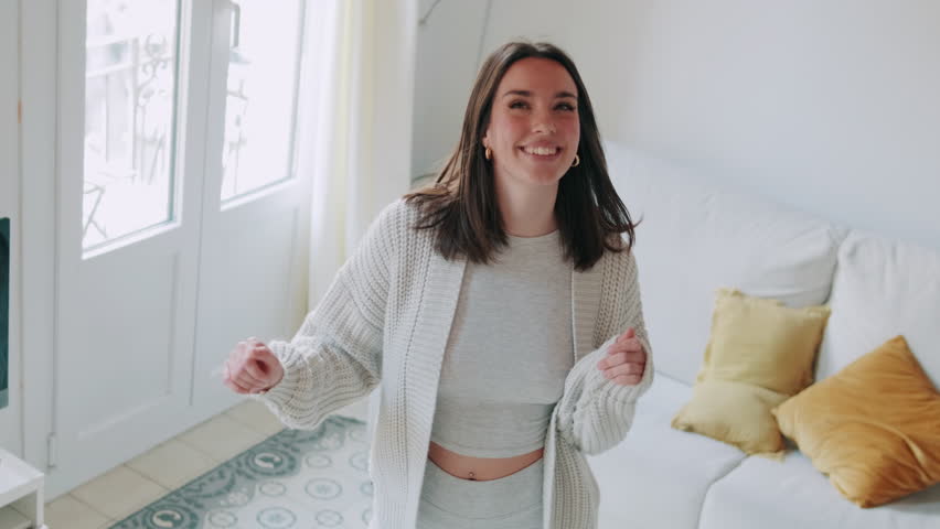 Carefree young woman dancing at home in her living room. She is happy, joyful, and enjoying life.