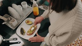 A woman spreads avocado on toast in the kitchen, orange juice in the background. She is making a healthy, nutritious breakfast. - Powered by Shutterstock - Get 15% off with code: PIKWIZARD15