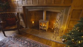 A cozy living room with a fireplace and a chair. The fireplace is lit and there are candles on it. A Christmas tree is also present in the room - Powered by Shutterstock - Get 15% off with code: PIKWIZARD15