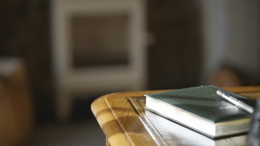 A book and pen are on a wooden table. The book is open to a page with a word on it. The scene is simple and uncluttered