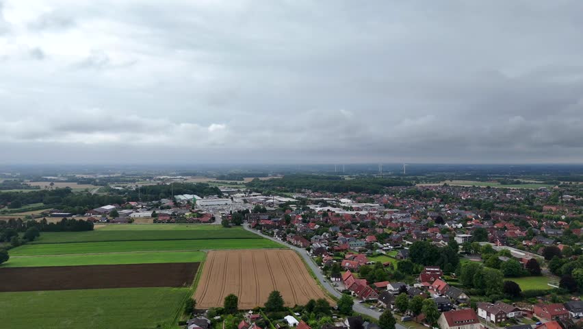 Rural farm fields in countryside of American town. Suburb district with houses and homes in with Dakota. Wind turbines and industrial district in background. Cloudy summer day. Aerial wide shot.
