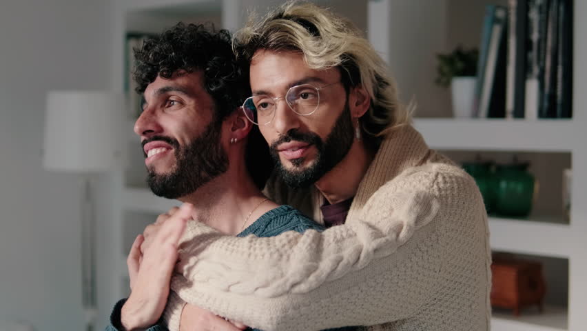 A happy gay couple is embracing and showing their love for each other in their modern apartment.