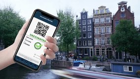 A hand holding a smartphone displaying a digital vaccination record, featuring a QR code and a green checkmark, with the picturesque canals of Amsterdam in the background. A blend of health tech and b - Powered by Shutterstock - Get 15% off with code: PIKWIZARD15
