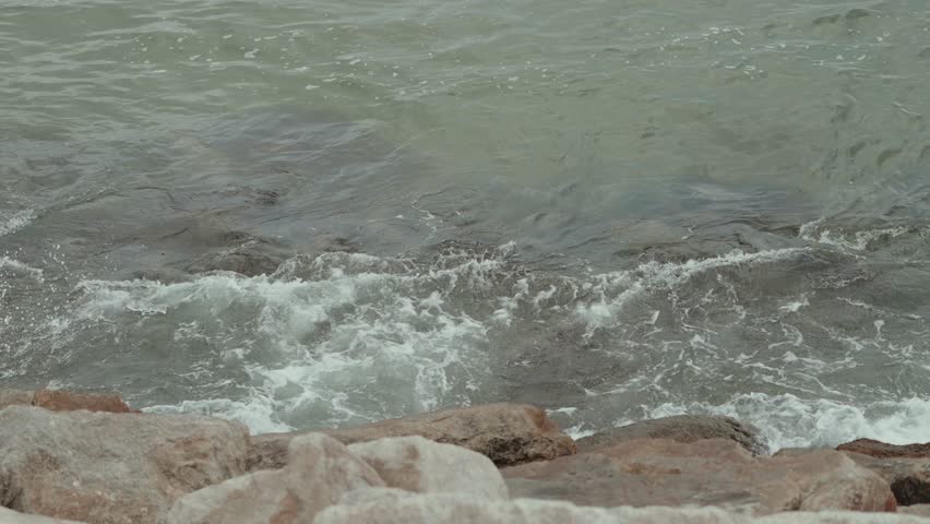 ocean waves splash against rocks in moody overcast light