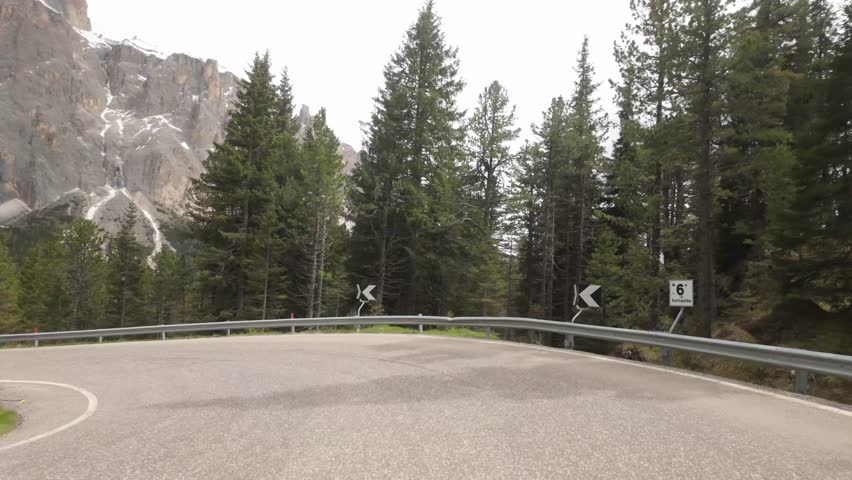 Warning signs mark a sharp curve on Giau Pass as the winding road stretches ahead into the Dolomites, framed by towering alpine peaks and dramatic terrain.