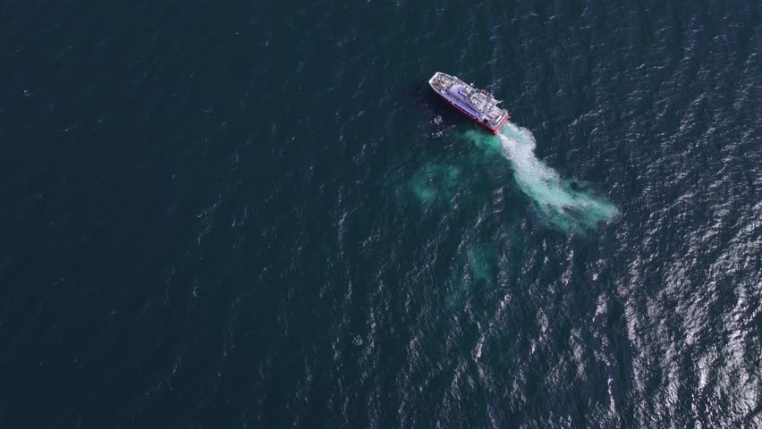 Serene aerial view of a deep blue ocean with boats scattered across the water. A larger vessel moves forward, leaving a faint trail behind.
