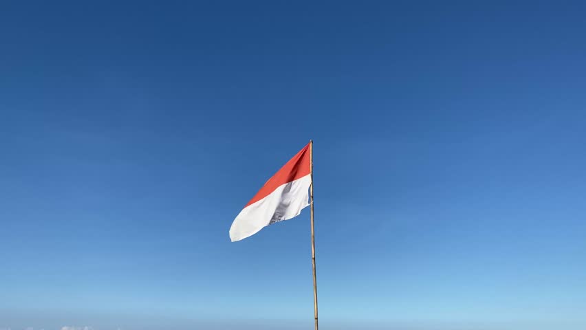 The flag of the Indonesian state that flutters against clear blue sky background. Usually flown on Independence Day on August 17th.	