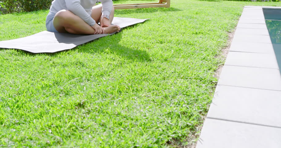 Mid adult Asian woman holding butterfly pose, stretching arms on backyard yoga mat for flexibility. Fitness, wellness, outdoor, tranquility, relaxation, mindfulness, rejuvenation