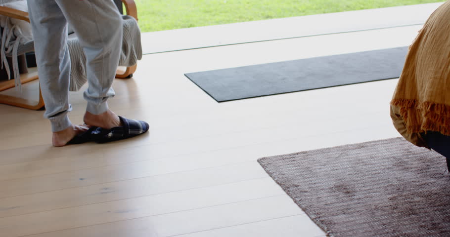 Stepping onto yoga mat Asian man folding forward, twisting torso by sliding glass doors for stretch. Meditation, wellness, flexibility, serene, leisure, outdoor, mindfulness
