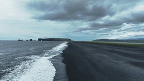 Aerial view of Reynisfjara's black sand beach with ocean waves, basalt sea stacks, and an overcast sky. The camera moves along the rugged coastline. - Powered by Shutterstock - Get 15% off with code: PIKWIZARD15