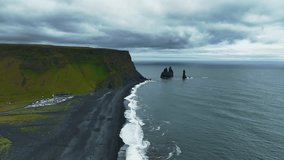 A sweeping aerial view of Reynisfjara's black sand beach, basalt sea stacks, ocean waves, green cliffs, parked vehicles, and visitors along the coastline. - Powered by Shutterstock - Get 15% off with code: PIKWIZARD15