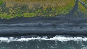Aerial view of a black sand beach in Iceland, showing waves crashing and retreating, with green vegetation framing the dynamic coastal scene. - Powered by Shutterstock - Get 15% off with code: PIKWIZARD15