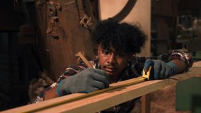 Young African American carpenter measuring and marking wood with tape and pencil inside a timber workshop, highlighting craftsmanship, precision, and manual woodworking skills. - Powered by Shutterstock - Get 15% off with code: PIKWIZARD15