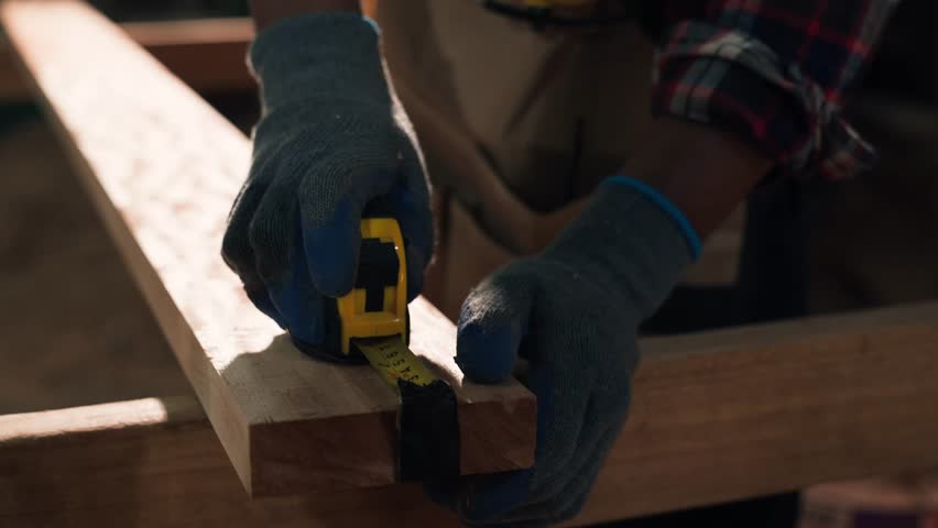 Young African American carpenter measuring and marking wood with tape and pencil inside a timber workshop, highlighting craftsmanship, precision, and manual woodworking skills.