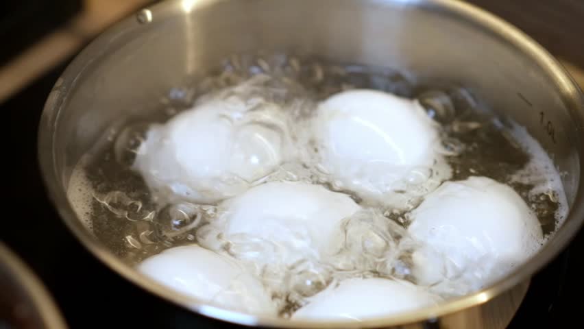 Water bubbles vigorously as eggs cook in a pot on the stove, demonstrating the technique for achieving the ideal hard or soft boiled eggs.