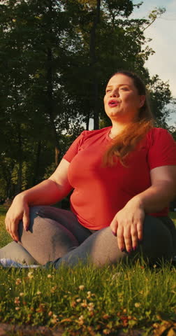 Outdoor Portrait of Body Positive Overweight Woman Doing Yoga Fitness Training Outdoors at City in the Morning, Plus Size Female Sitting Relaxed on Yoga Mat. Vertical Video