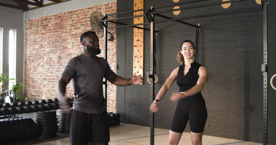 Diverse trainer and trainee at gym performing arm swings then triceps stretch with pull-up rig. Fitness, strength, mobility, workout, training, athletic, health