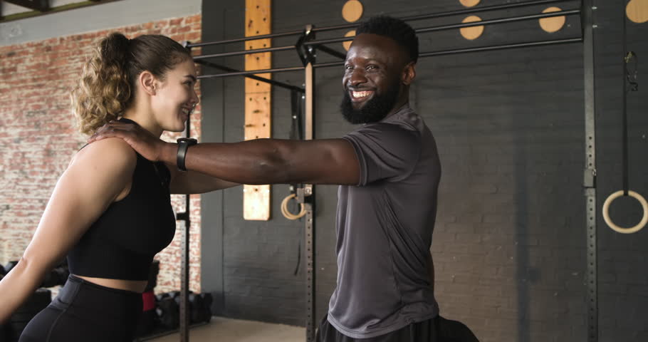 African American trainer guiding White woman through quad stretch getting ankle hold at gym rig. Fitness, training, motivation, strength, athleticism, wellness, sport