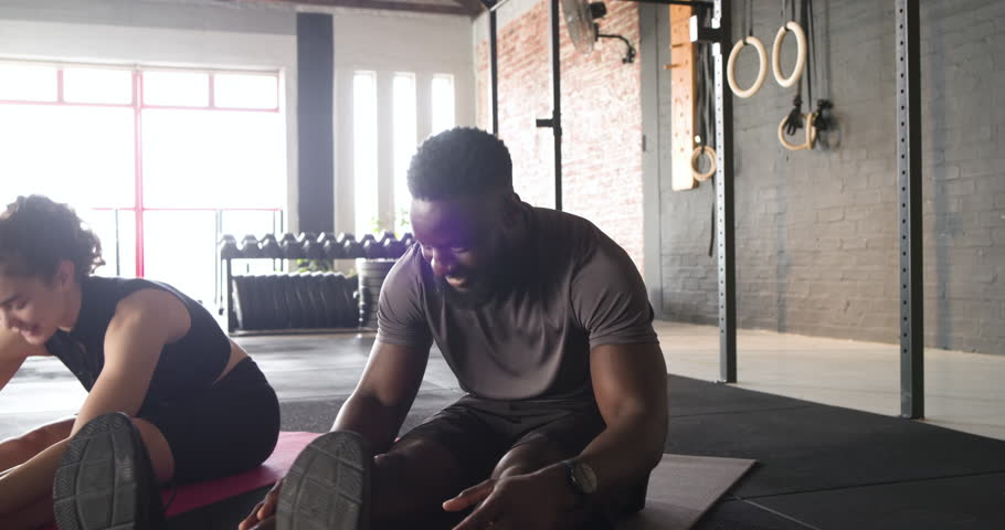 Diverse exercise partners settling on mats repeating hamstring stretch cycle at gym for flexibility. Stretching, flexibility, partnership, fitness, wellness, endurance, body movement