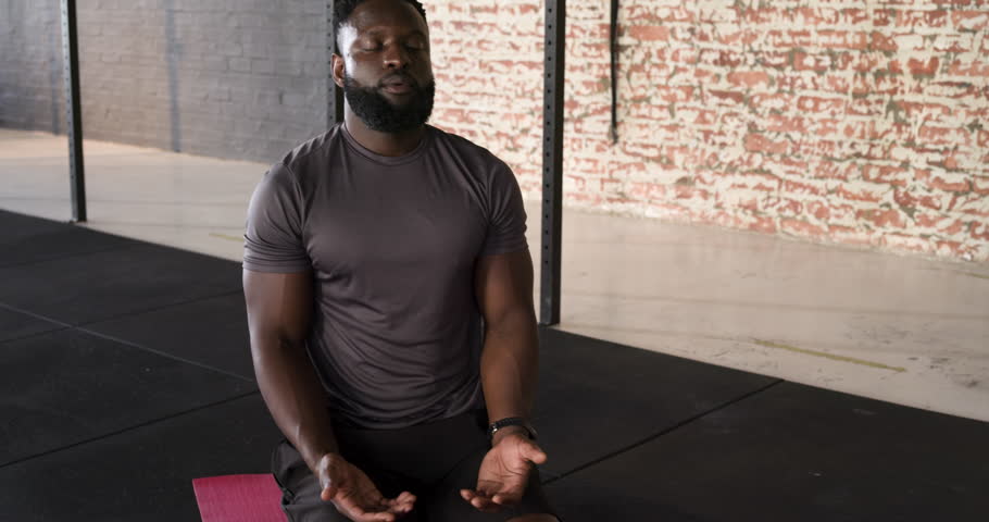 African American man raising palms, inhaling and exhaling for focus on rose mat in workout studio. Meditation, mindfulness, wellness, fitness, tranquility, stretching, concentration