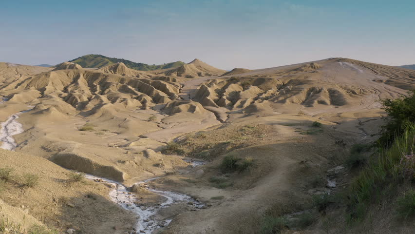 A man dressed in white stands in the wilderness, looking ahead at a sandy mountain. Near him is a stream flowing through the hills.