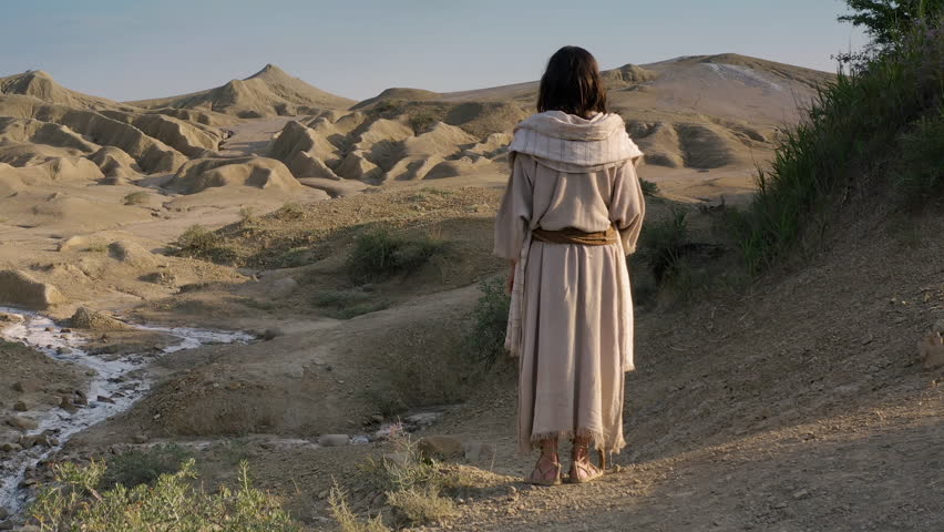 A mysterious man in a white robe following the path through the sandy mountains of the Judean wilderness. Large crane shot