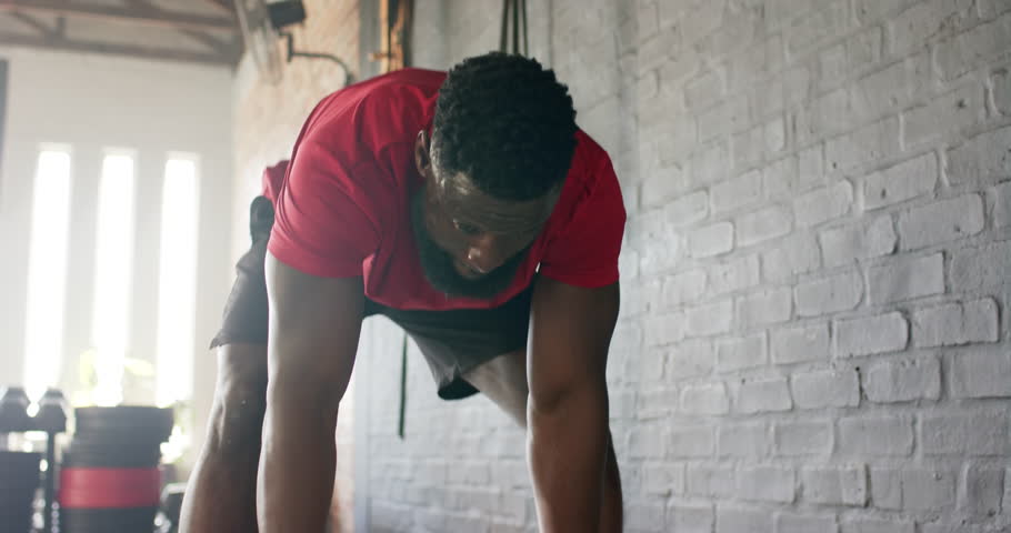 African American man in red gear entering gym gripping ball lifting, throwing at wall for strength. Fitness, strength, endurance, workout, training, athleticism, exercise