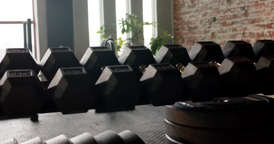 Camera is panning right-to-left in loft gym showing hexagon dumbbells on rack and sled by window. Fitness, strength, industrial, modern, interior, urban, workout